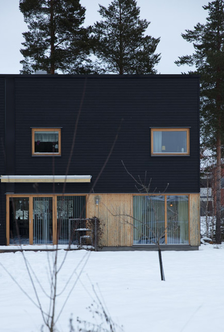 Scandinavian style black house with natural wood in snowy natural area