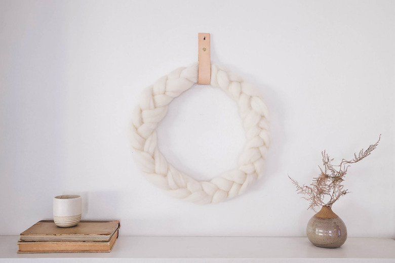 DIY braided ivory wool wreath hung on wall with leather strap