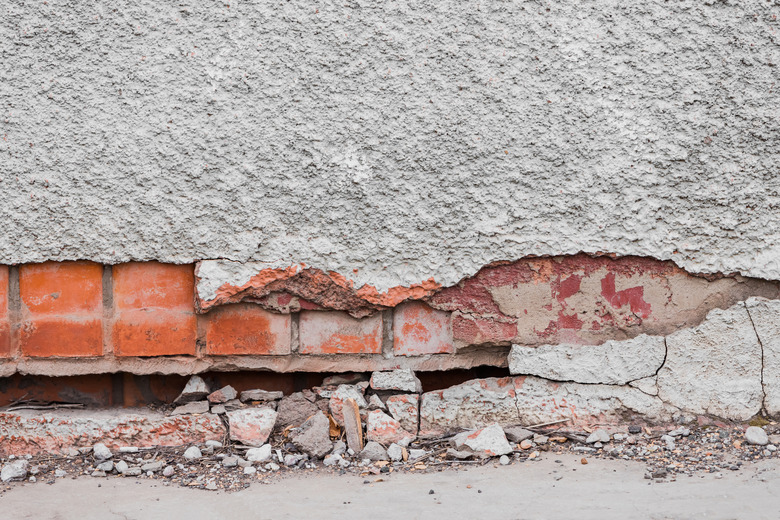 The foundation of a residential building is gradually collapsing. Cracks in the foundation. Plaster falling off of a brick wall due to the impact of weather factors.