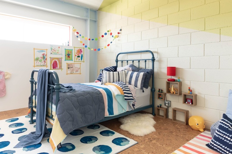 Kid's bedroom corner with yellow walls, blue bedding, primary color banner, and watercolor circle rug