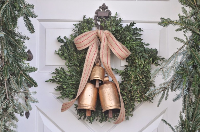 Christmas Door Decorations with Evergreen wreath with gold bells and ribbon on white door.