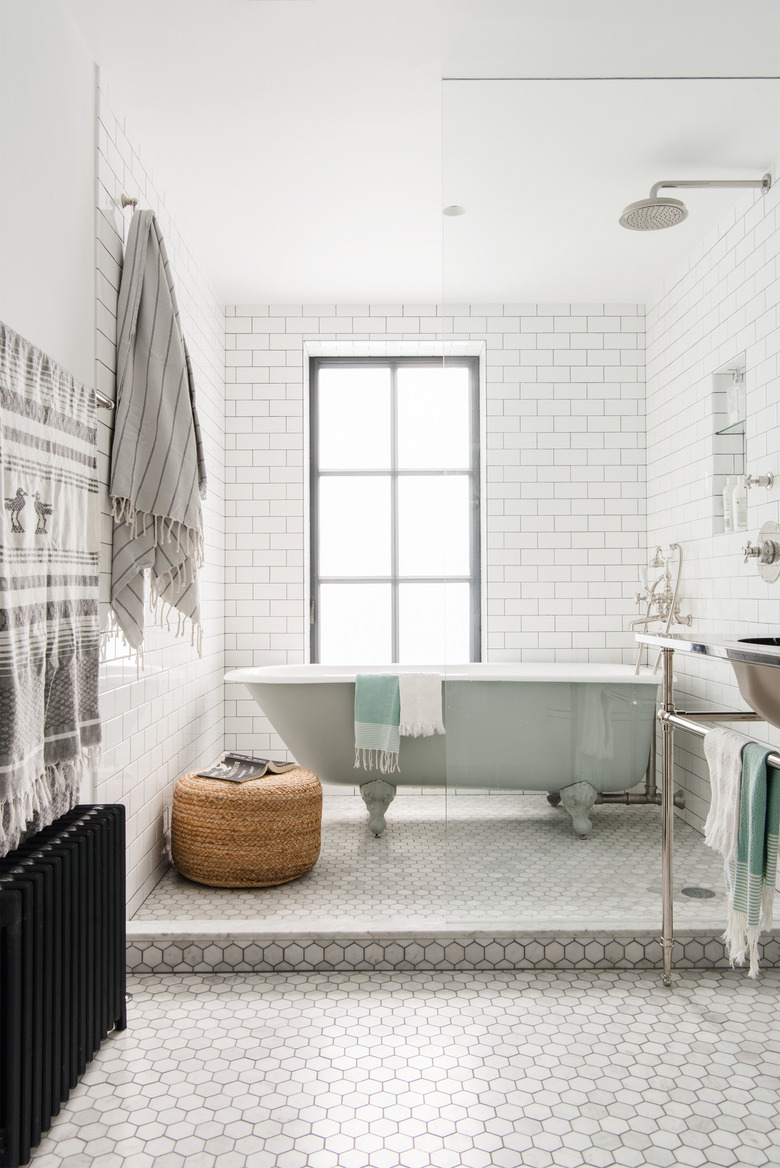 white modern bathroom with freestanding clawfoot tub and a window behind it