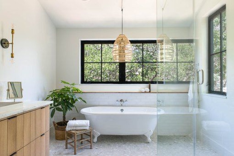 white modern bathroom with freestanding clawfoot tub in front of a wall with windows