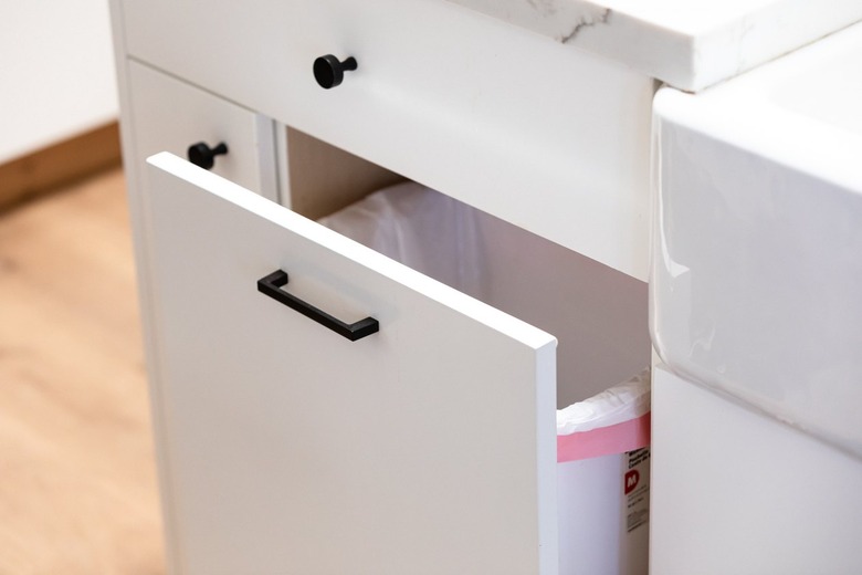 white kitchen cabinet with pull out trash can