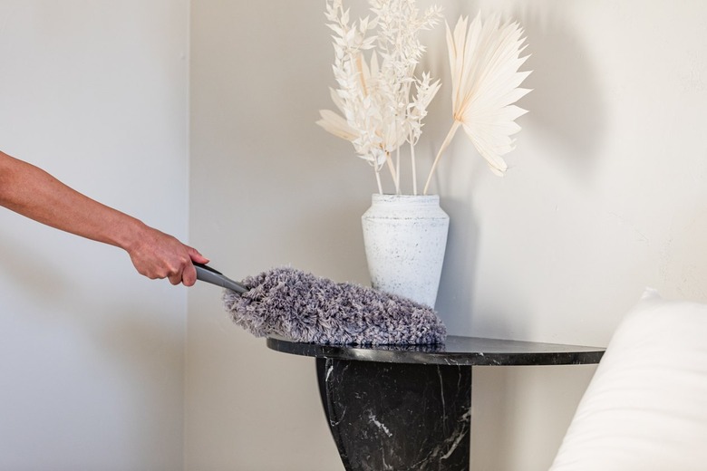 A person dusting a black half moon side table with a vase of dried florals