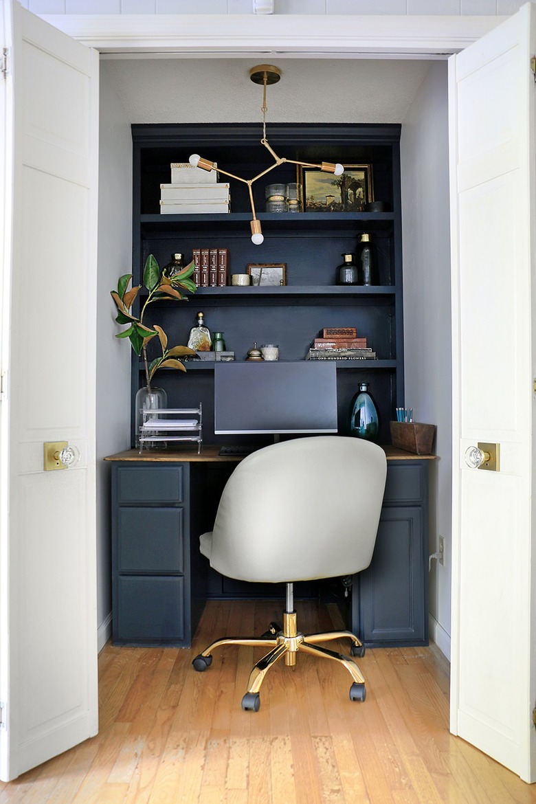 white closet office with black built-in desk and shelves with gray swivel chair