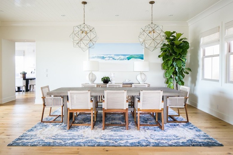 coastal dining room with oversize plant and woven dining chairs