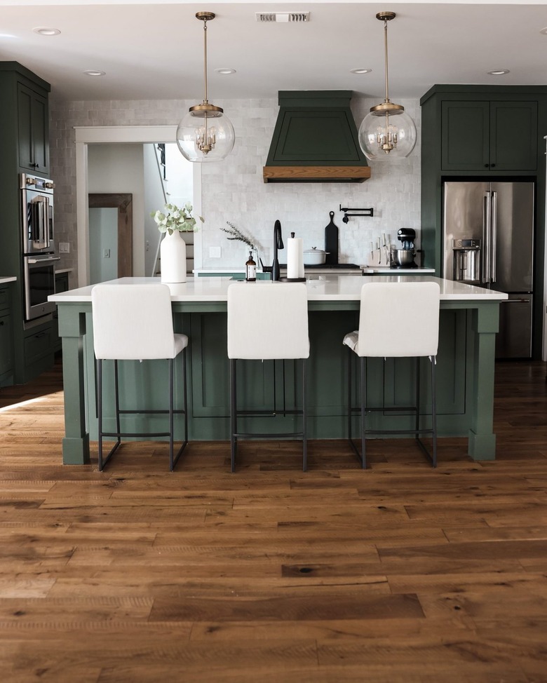 Dark sage green kitchen cabinets and white barstools