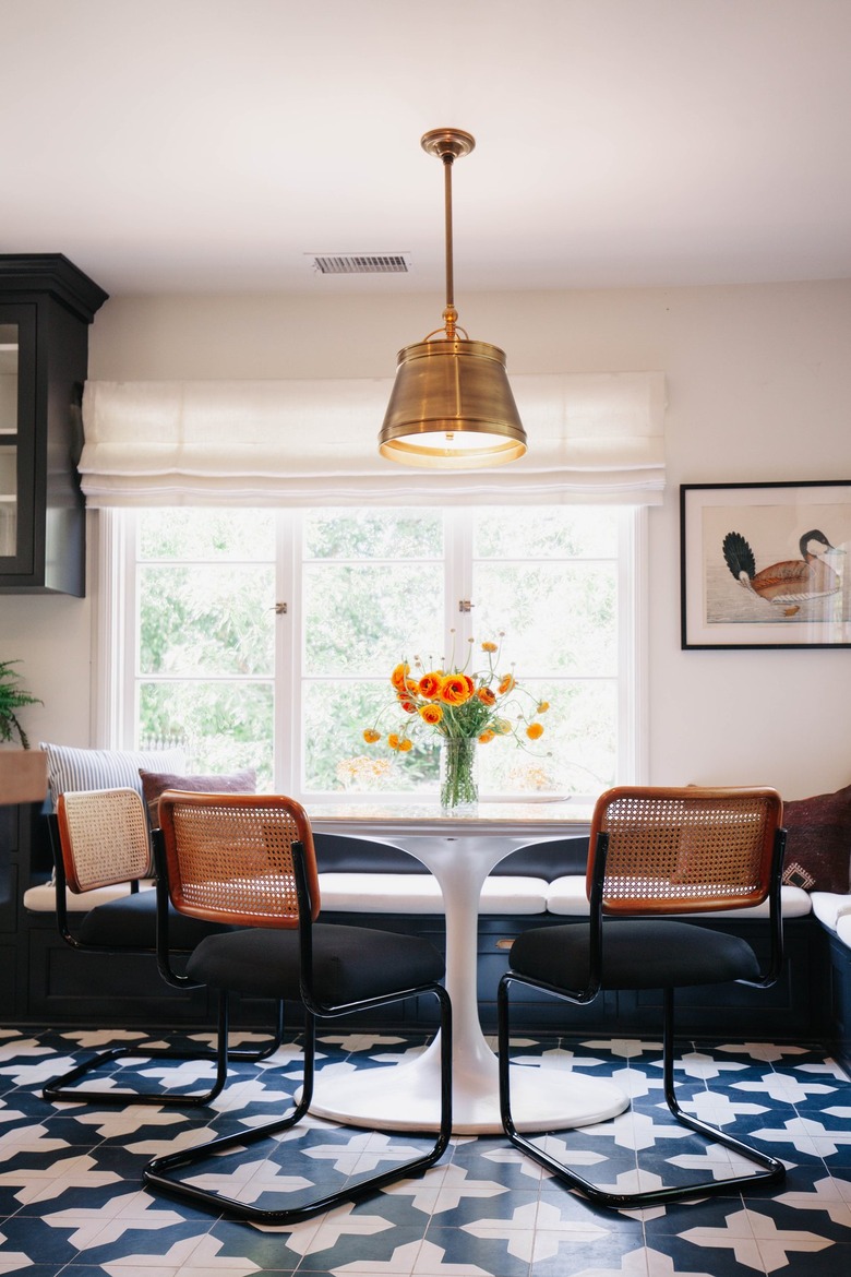 Dining room with flute table, cane chairs, ornate tile floor, pendant light and indoor upholstered bench