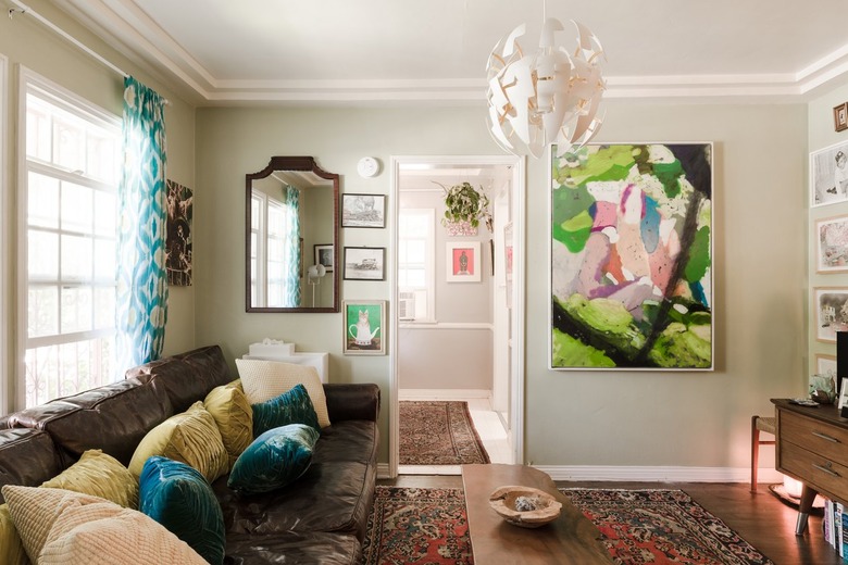 Colorful living room with leather sofa with blue and neutral pillows, eclectic art, layered pendant light, wood furniture, and traditional rug.