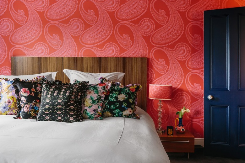 red wallpapered bedroom with woodgrain headboard and floral throw pillows