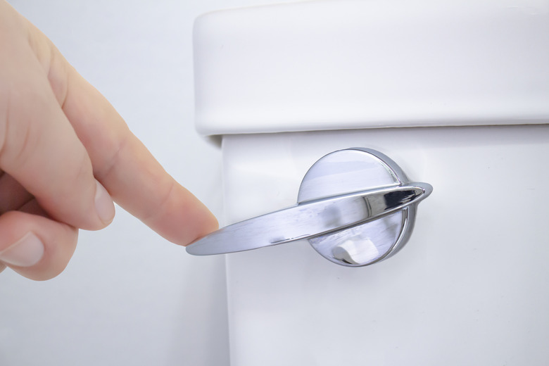 A person flushing a toilet on a washroom.