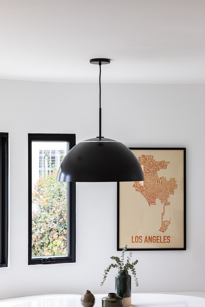 Black contemporary dining room lighting against curved white wall with framed print and window above round white table with plants