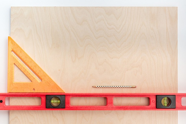 using a level and a speed square to mark where a shelf will go on a plywood sheet