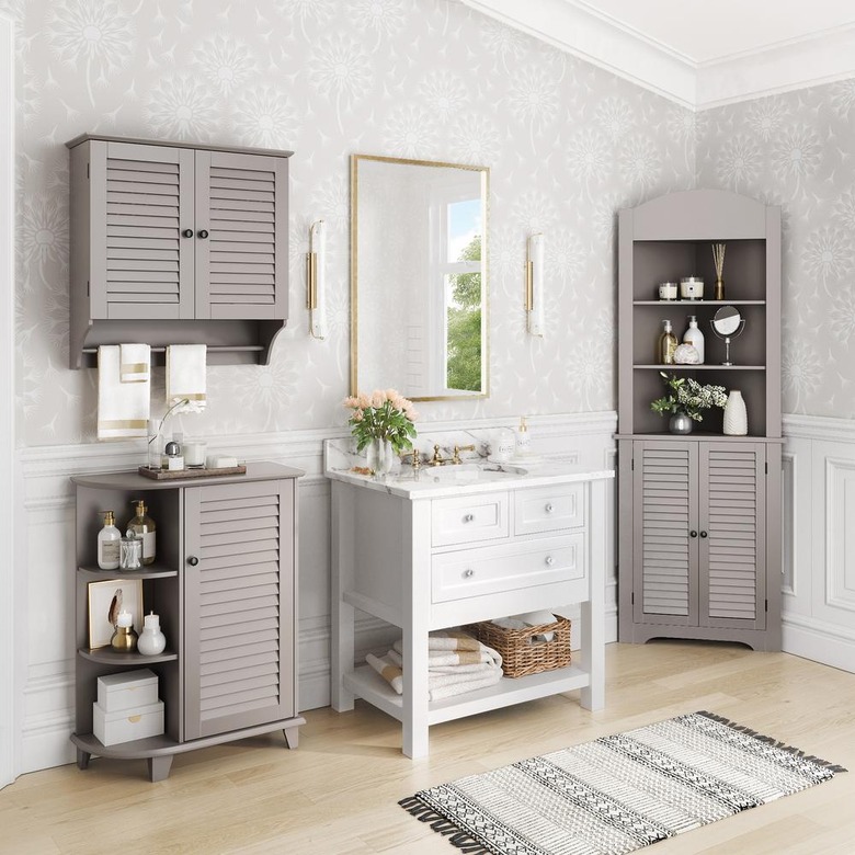 Taupe corner bathroom cabinet and white sink in wallpapered bathroom with hardwood floors