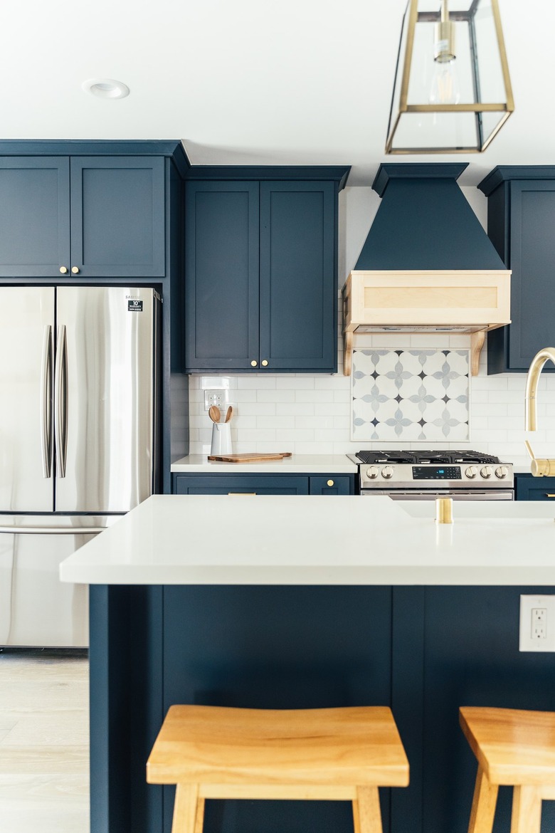 Kitchen with dark blue cabinets, French refrigerator, ornate backsplash by stovetop, kitchen island with wood stools, lantern pendant light