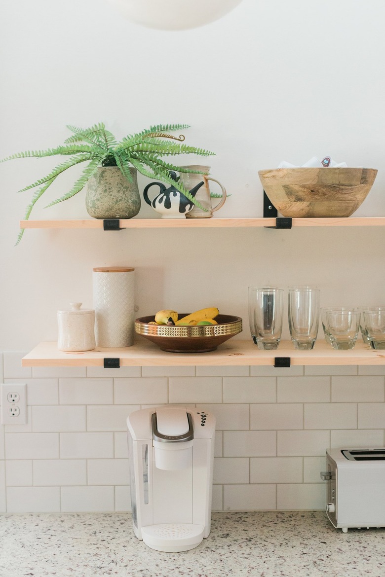 Wood shelving with dishware and plant with white tile wall and appliance