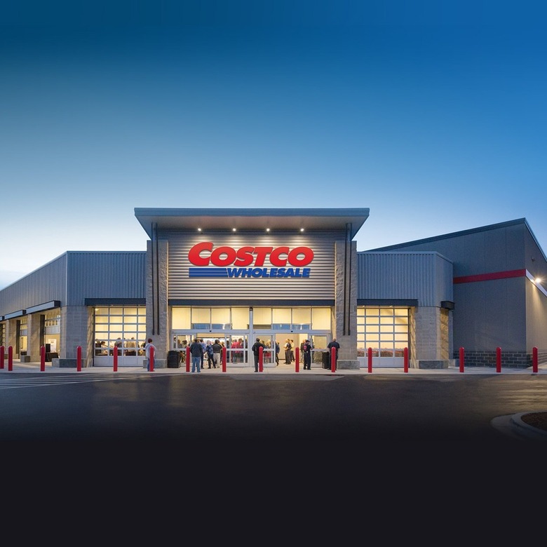 The exterior of a Costco warehouse at twilight. There is a red and blue sign at the front that says 