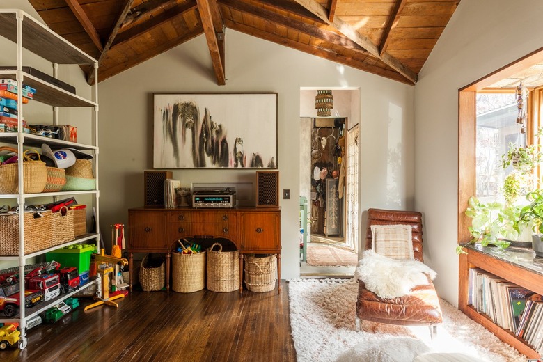 Craft Storage in Living room with lounge chair, sheepskin thrown, rug, shelves with baskets and toys, baskets on floors, credenza, stereo, wood floors, records, arched wood ceiling.