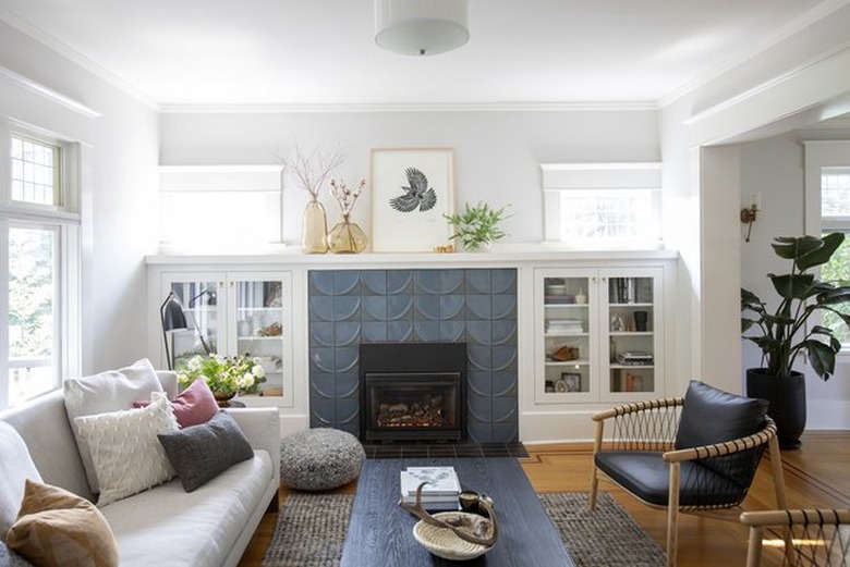 tiled Craftsman style fireplace in living room surrounded by white cabinets