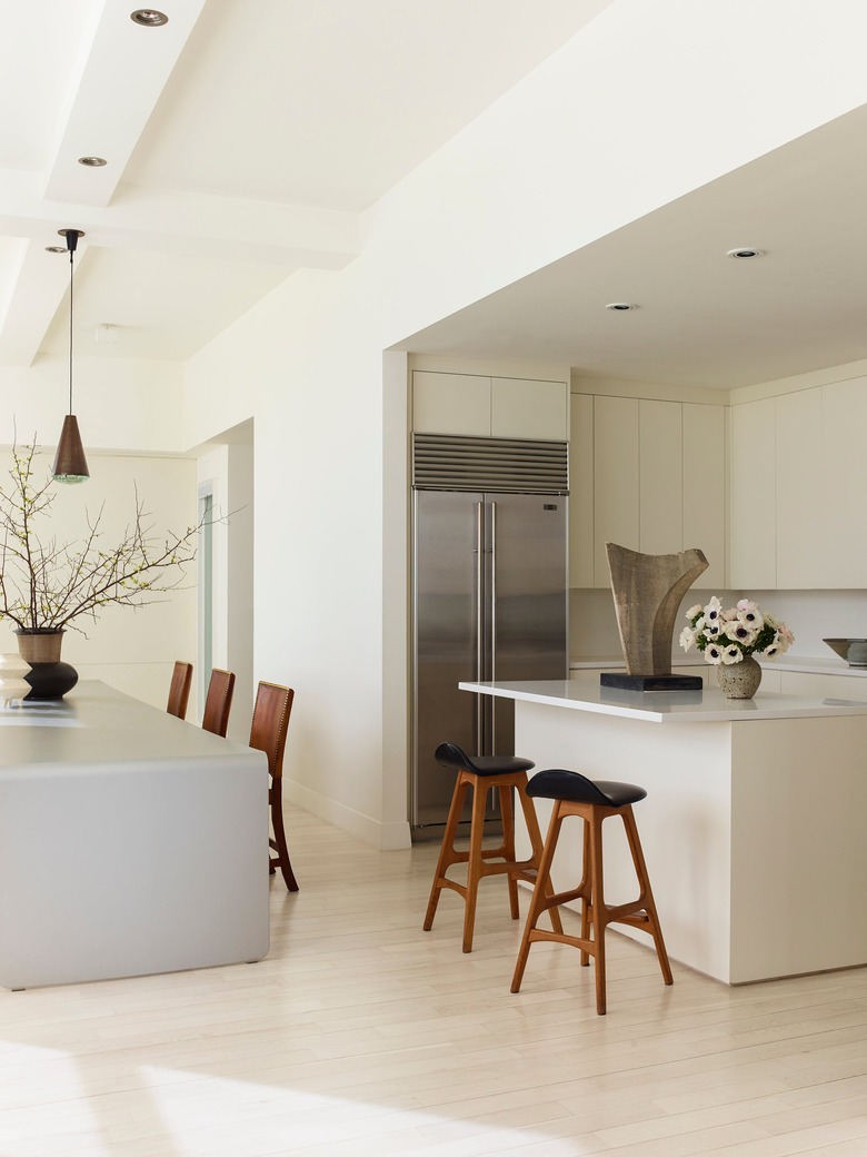 Modern kitchen with pale wood floors and cabinetry and high ceilings with recessed lighting and pendant light over table