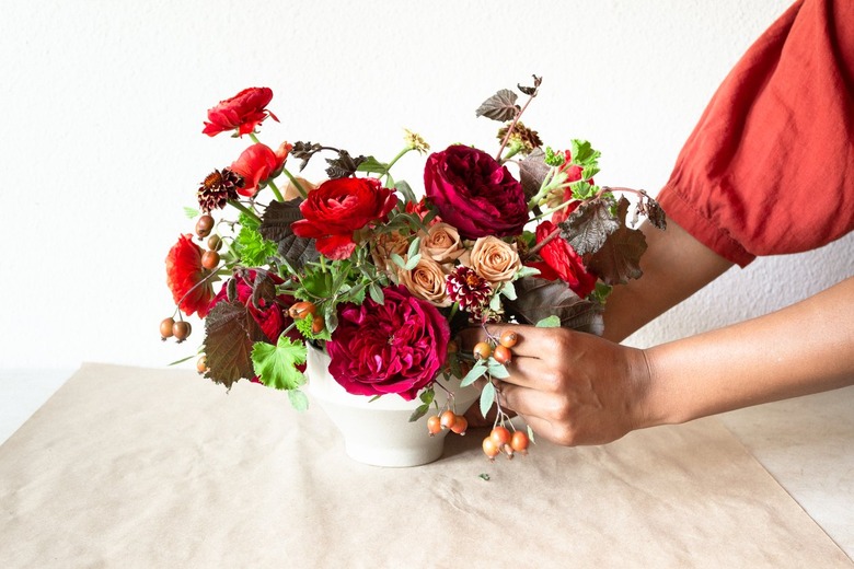 a diy floral centerpiece made of caramel roses and red flowers  including ranunculus and zinnias