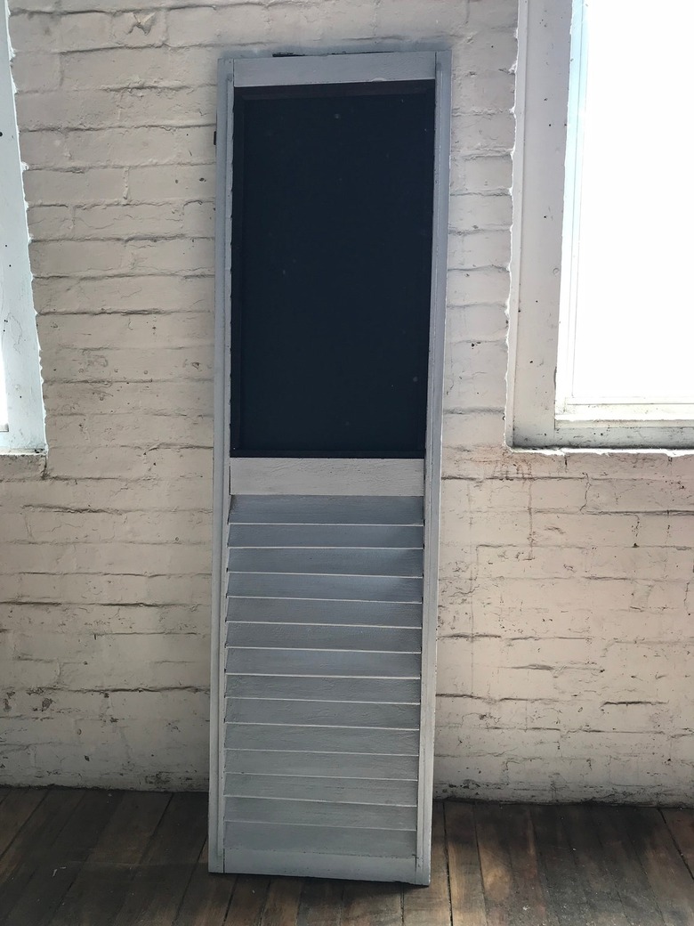 Repurposed gray antique shutter with chalkboard paint against white brick wall