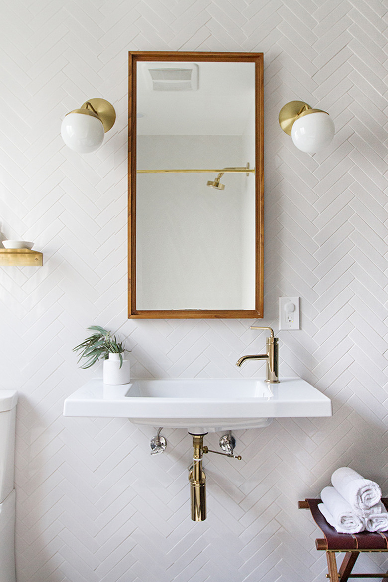 thin wall-mounted bathroom sink on herringbone wall tile and brass fixtures