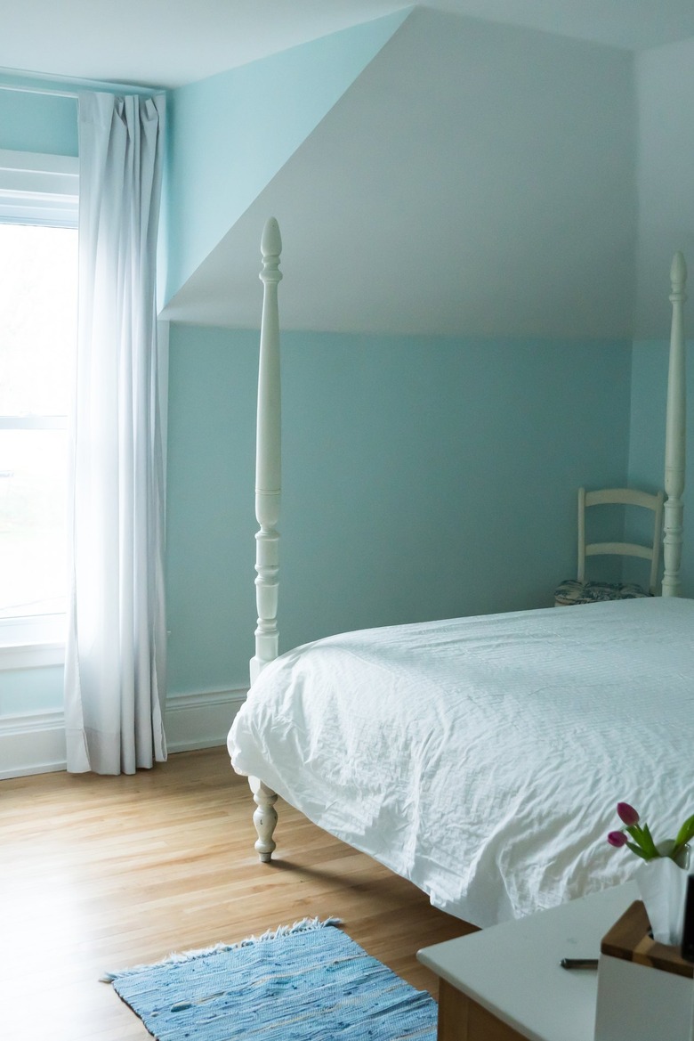 a bed with a white bedspread and white bed posts in a room with light green walls and a narrow-plank floor