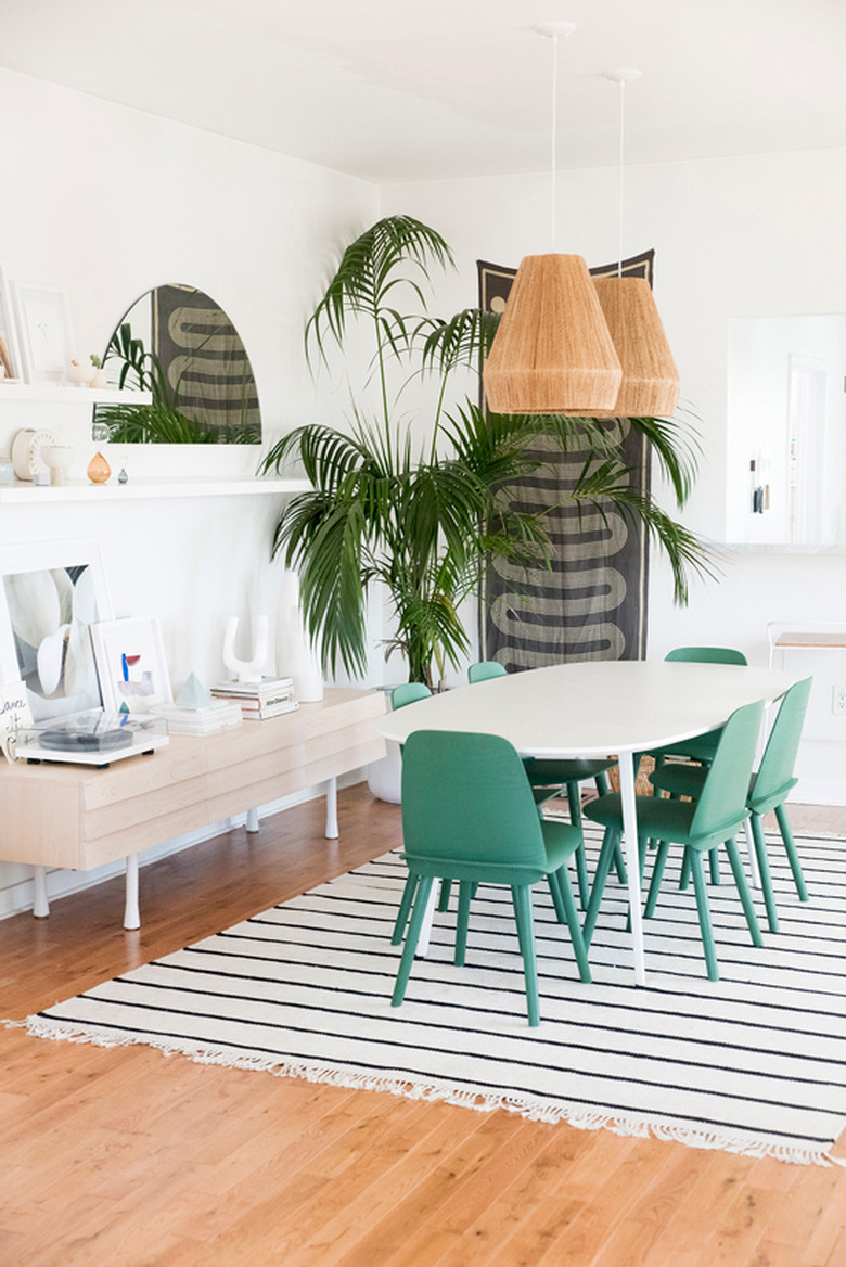 bohemian dining room idea with large potted plant and woven pendant lights above table with green chairs