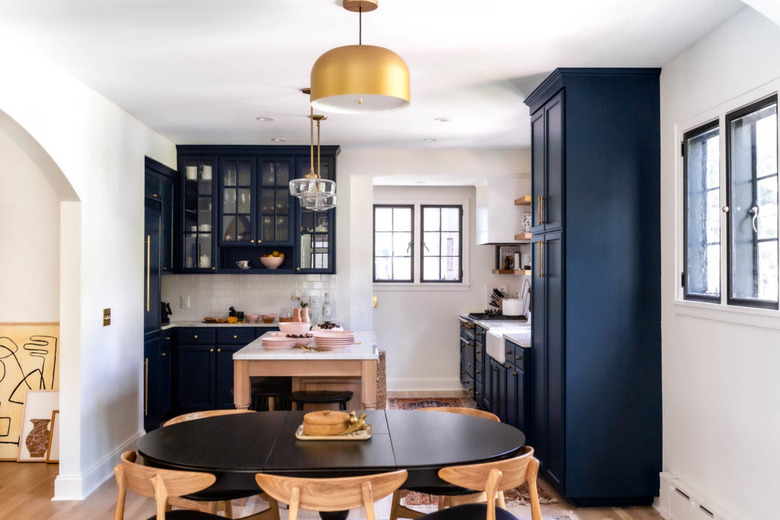 dining room lighting idea with brass pendant hanging over oval table near kitchen with blue cabinets