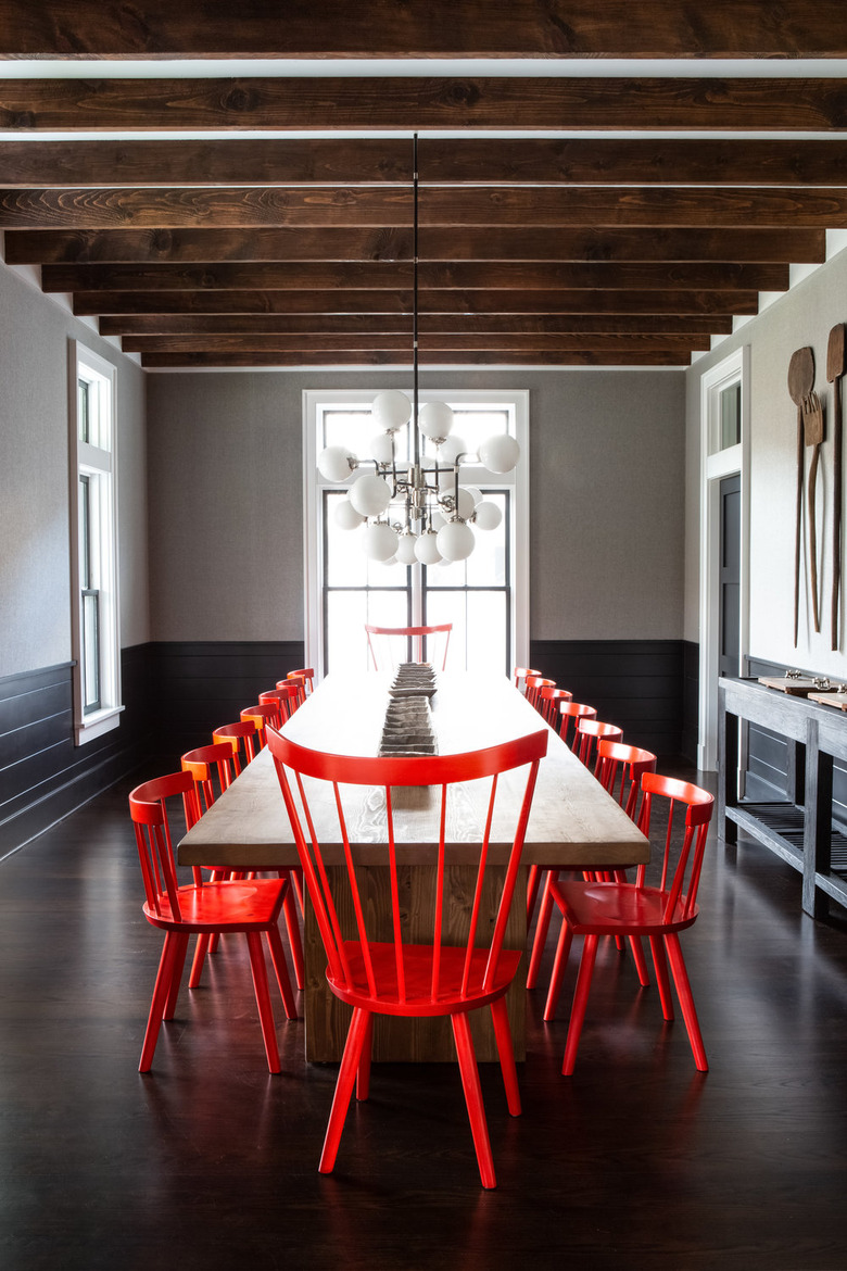 black dining room wainscoting with red chairs and wood beams by Chango & Co.