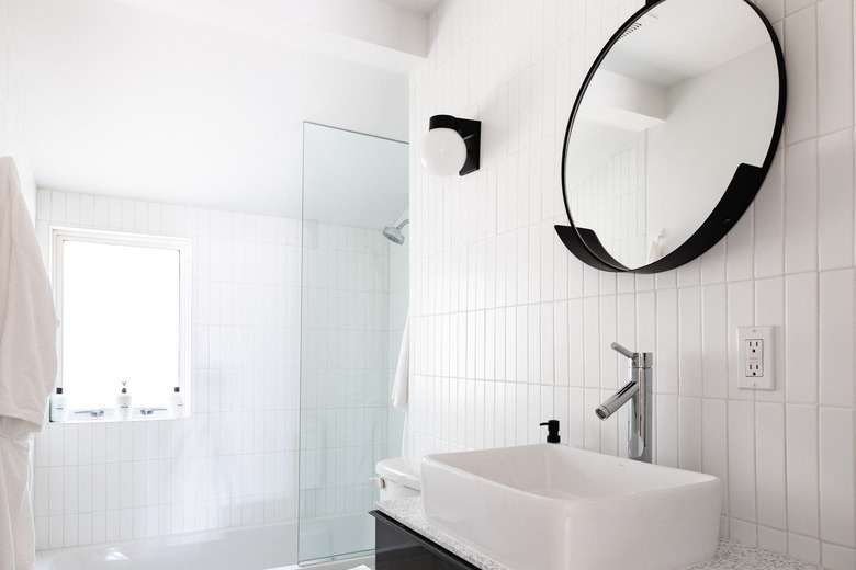 White tile in bathroom with round black mirror