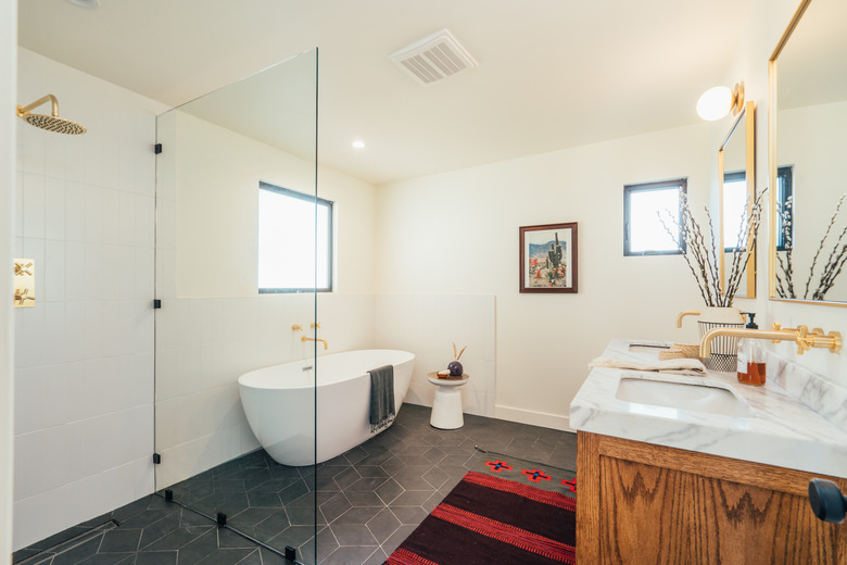 bathroom with standing shower with glass wall, stand-alone white tub and natural wood and stone top bathroom vanity with brass faucets