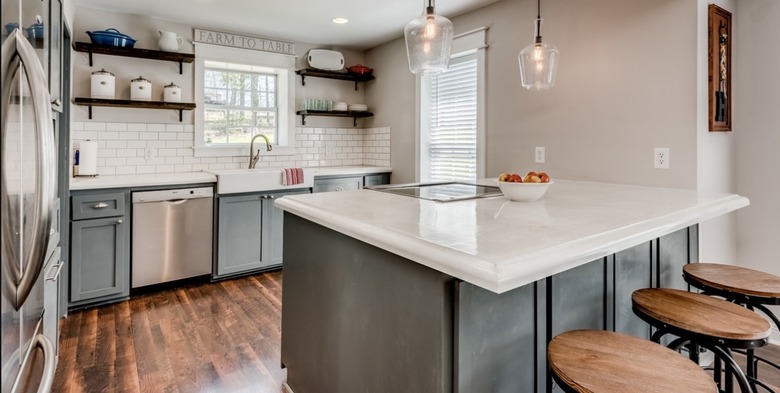 Modern kitchen with open wood shelving, gray cabinets, island and white concrete countertops.