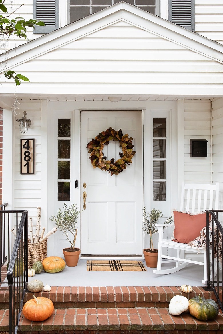 Porch decorated for fall with pumpkins, wreath, logs and rocking chair