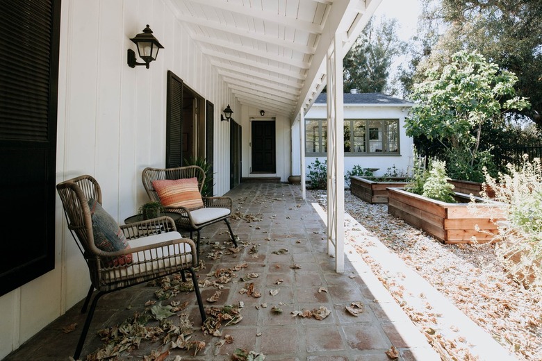 Porch with with vault overhang and black lantern sconce and wicker chairs facing boxed garden beds