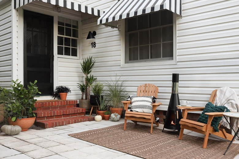 Porch area decorated for fall with outdoor furniture, a fireplace, and plants