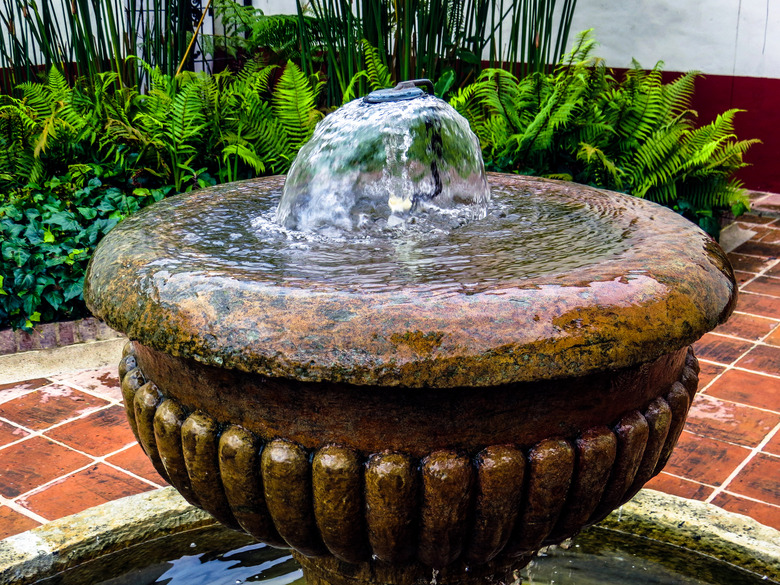 Top of antique water fountain with garden in background