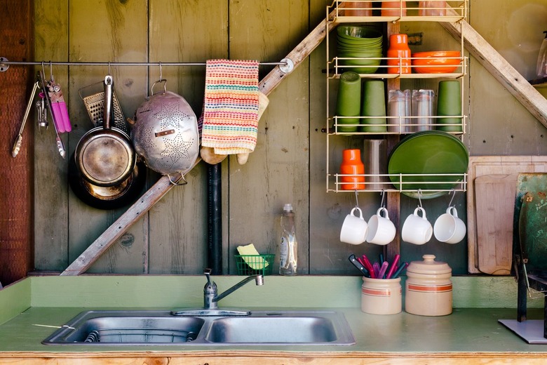 a small outdoor kitchen with wall-mounted racks for cups and plates and pots hanging from a rod