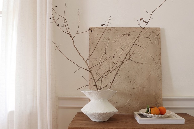 DIY paper mache vase with dried branches on cabinet next to bowl of oranges