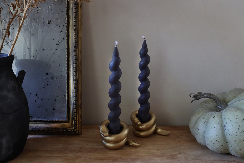 DIY gold snake candleholders with black spiral taper candles on table with pumpkin and mirror