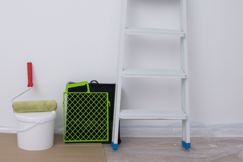 against the background of a white wall, there is a step ladder, a roller bath and a bucket of paint