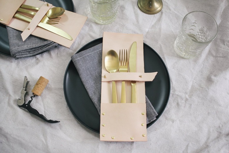 a leather flatware pocket holding gold utensils on a black plate