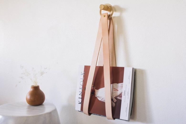 Leather strip magazine holder with wood hoop next to table with brown vase