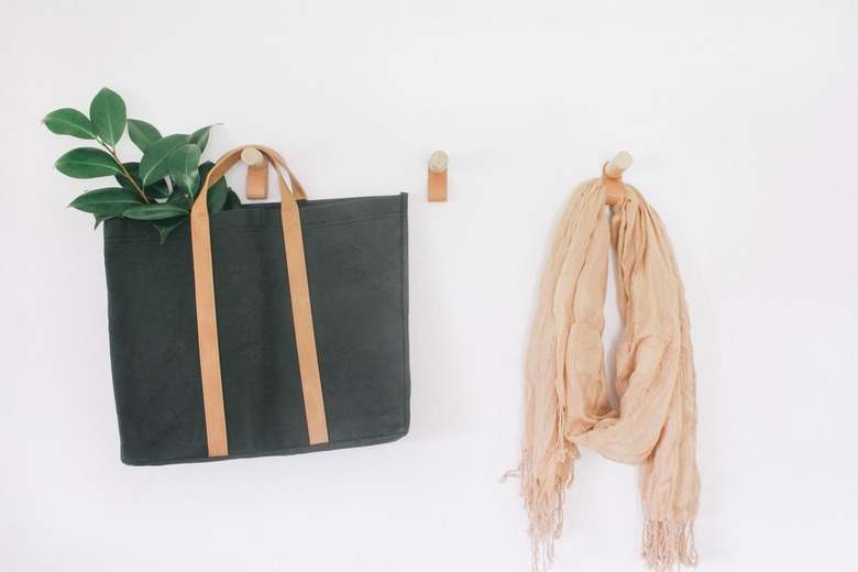 three coat hooks made from thick wooden dowels and a leather loop hanging below, with clothes and bags hanging from them