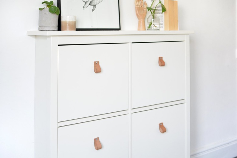 White dresser with leather pull handles on drawers with art and plants