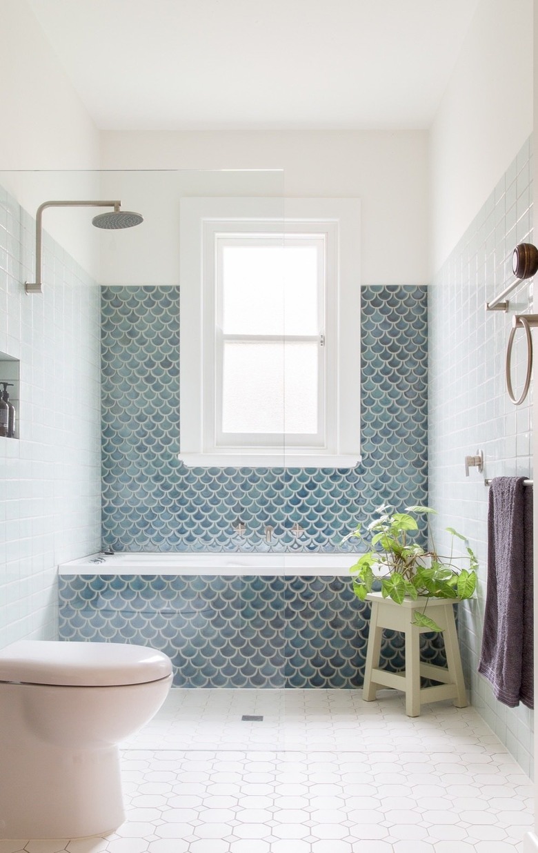 wet room with shower and small bathtub covered in blue fishscale wall tile