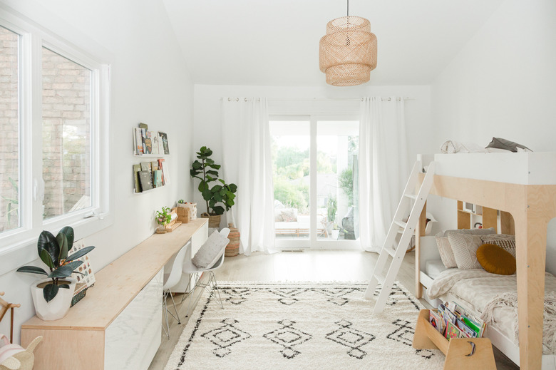 A child's bedroom with bunkbeds and sliding glass doors covered with white curtains