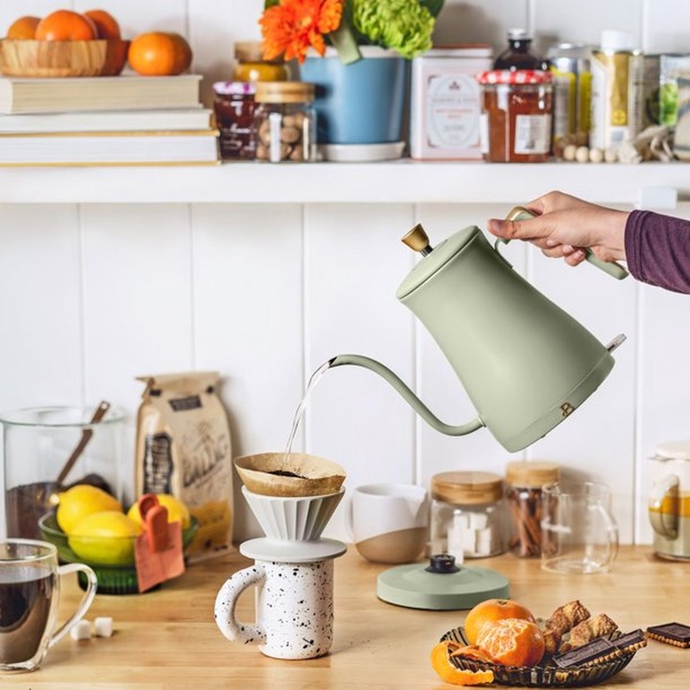 A hand holding a light green kettle and pouring hot water into a pour-over coffee.